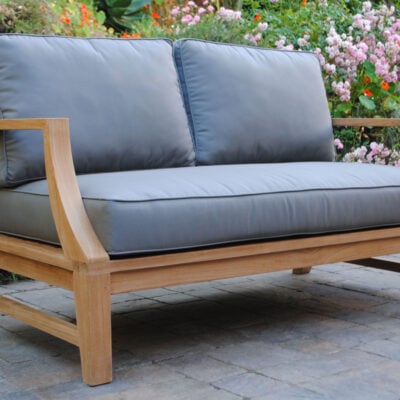 side angle view of teak Capitola Deep Seating Loveseat with gray Cushions with flowers in background Paradise Teak Bay Area California